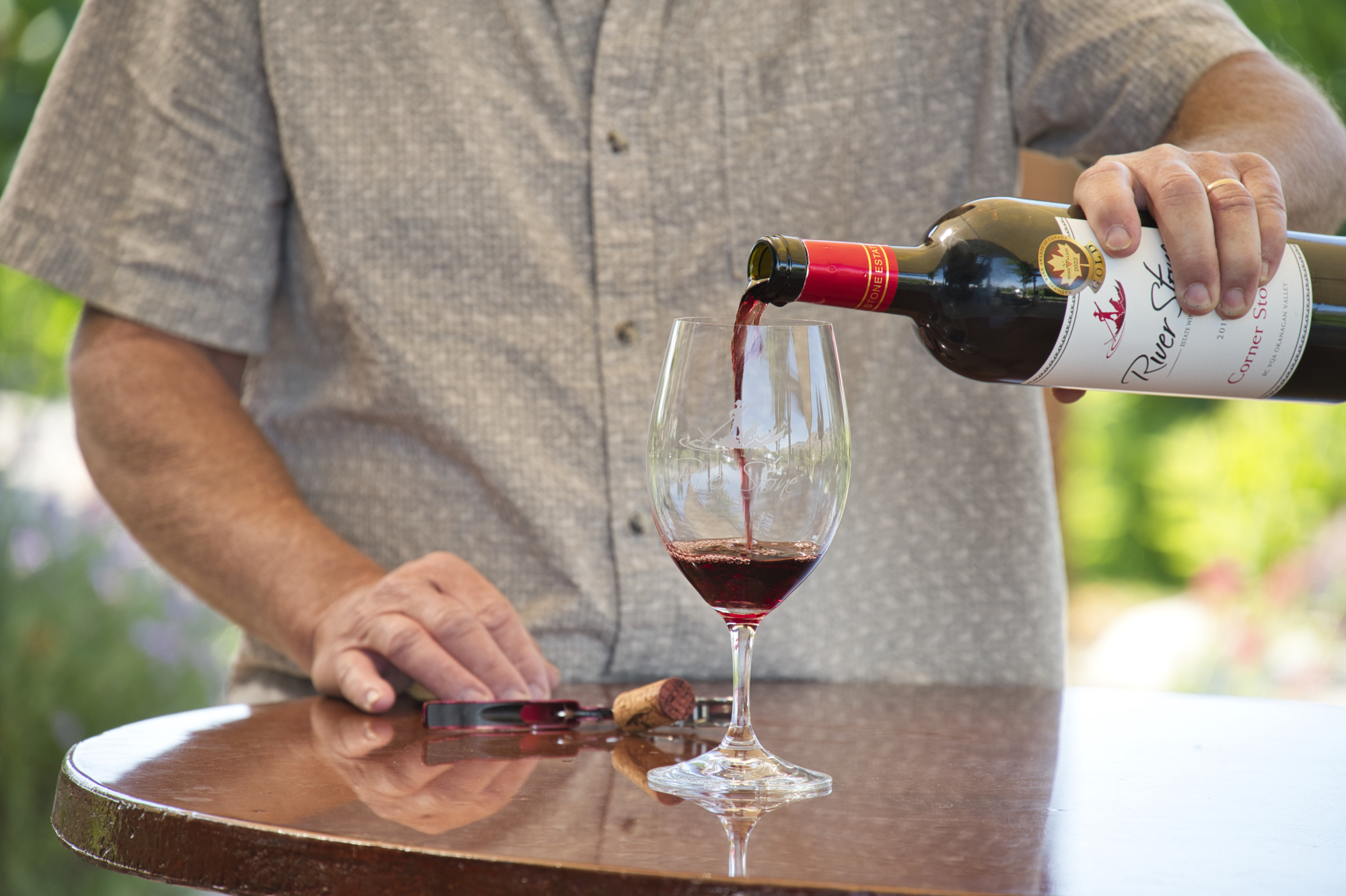 Person pouring a bottle of River Stone wine into a glass
